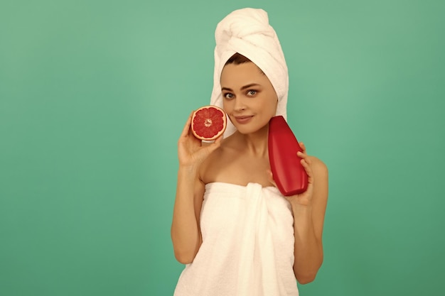 Hermosa mujer sonriente en toalla con botella de champú de pomelo sobre fondo azul.