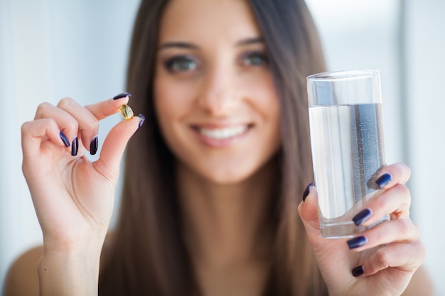 Hermosa mujer sonriente tomando píldora de vitaminas y suplemento dietético