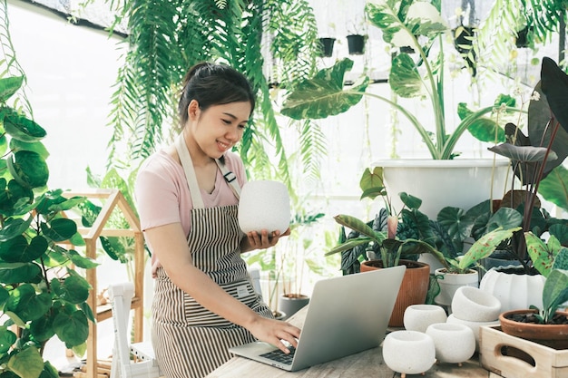 Hermosa mujer sonriente trabaja en la tienda minorista del centro de jardinería Tomando pedidos por teléfono Ella trabaja en la mesa y en el fondo hay una tienda con muchas plantas