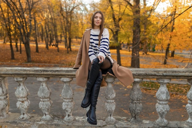 Hermosa mujer sonriente en traje elegante sentada en la mesa con un sombrero y un suéter romántico estado de ánimo feliz esperando a un novio en una cita en un café tendencia de la moda de primavera y verano tomando café