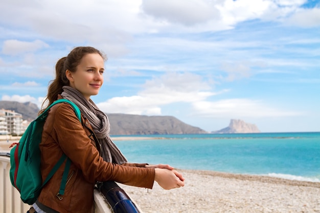 La hermosa mujer sonriente el turista de pie en la playa y disfrutando del sol primaveral y una vista del paisaje marino de Mediterranien.