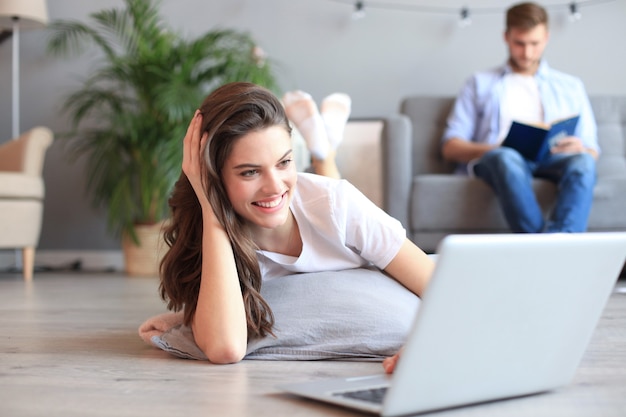 Hermosa mujer sonriente usando laptop con hombre borroso de fondo en casa.