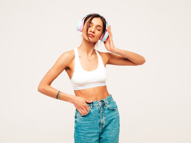 Hermosa mujer sonriente vestida con ropa de jeans. modelo despreocupado escuchando música en auriculares inalámbricos