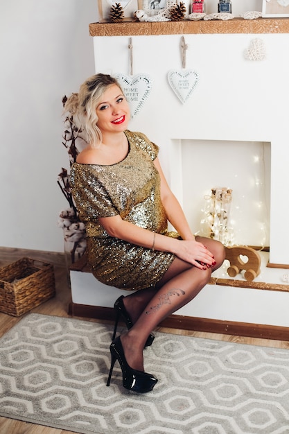 Hermosa mujer sonriente en vestido dorado brillante sentado en la chimenea.