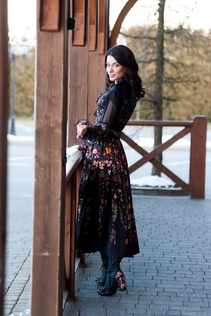 Hermosa mujer con sonrisa en vestido cerca de barandilla de madera
