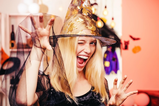 Hermosa mujer sorprendida con sombrero de bruja y disfraz Retrato de mujer de Halloween Bruja de Halloween con una calabaza tallada y luces mágicas en una habitación oscura Concepto de personas de Helloween