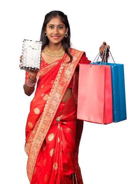 Hermosa mujer sosteniendo bolsas de compras y caja de regalo sobre un fondo blanco.