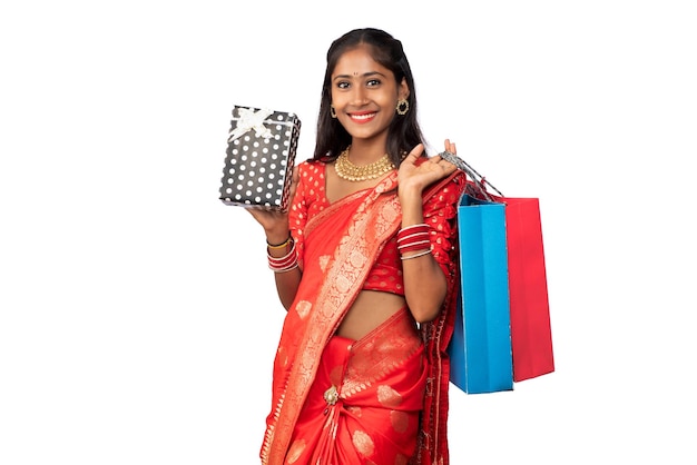 Hermosa mujer sosteniendo bolsas de compras y caja de regalo sobre un fondo blanco.