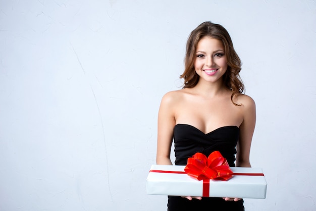 Hermosa mujer sosteniendo una caja de regalo blanca con cinta roja.