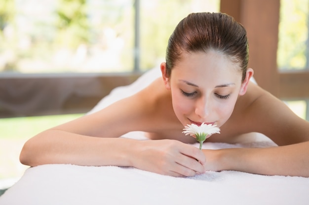 Hermosa mujer sosteniendo la flor en la mesa de masaje en el centro de spa