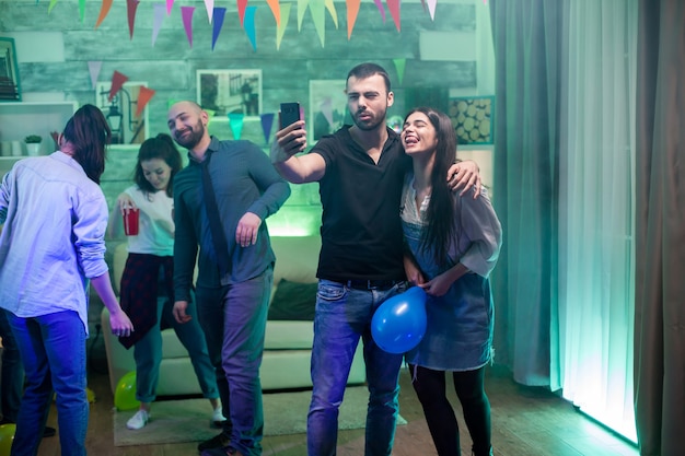 Hermosa mujer sosteniendo globo mientras toma un selfie en una fiesta con su amiga.