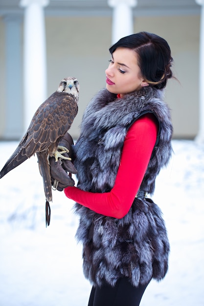 Hermosa mujer sosteniendo un halcón en su mano en invierno