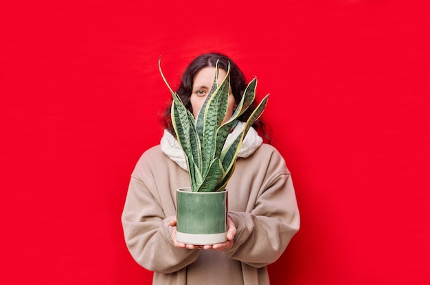 Una hermosa mujer sosteniendo una maceta con plantas de serpientes en la pared roja