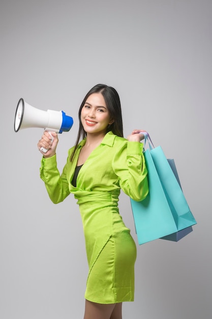 Hermosa mujer sosteniendo megáfono y bolsa de compras sobre estudio de fondo blanco