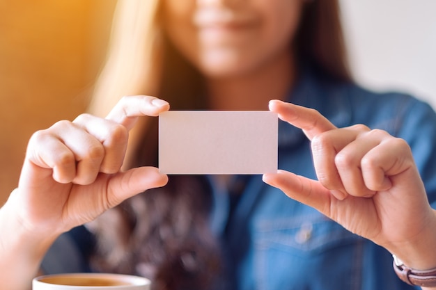 Foto una hermosa mujer sosteniendo y mostrando una tarjeta de presentación vacía en blanco a alguien