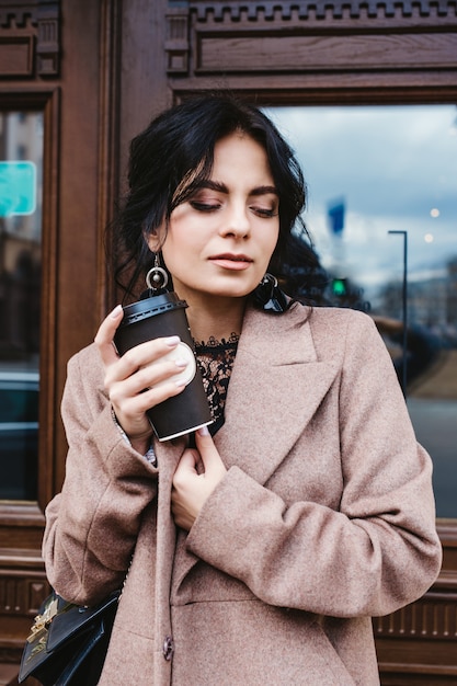 Hermosa mujer sosteniendo la taza de café de papel y disfrutando del paseo por la ciudad