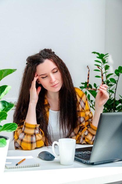 Hermosa mujer sostiene sus sienes debido a un dolor de cabeza o dolor en los ojos por trabajar en una computadora portátil