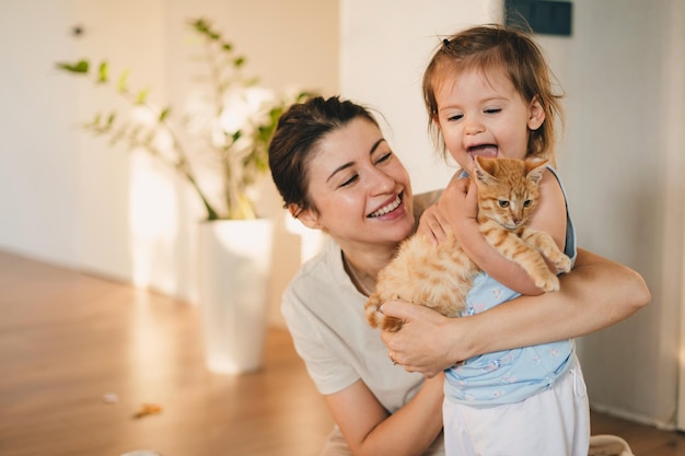 Foto hermosa mujer con su bebé en casa sosteniendo y abrazando a su encantador gato esponjoso amigo de humanos buenos días soleados