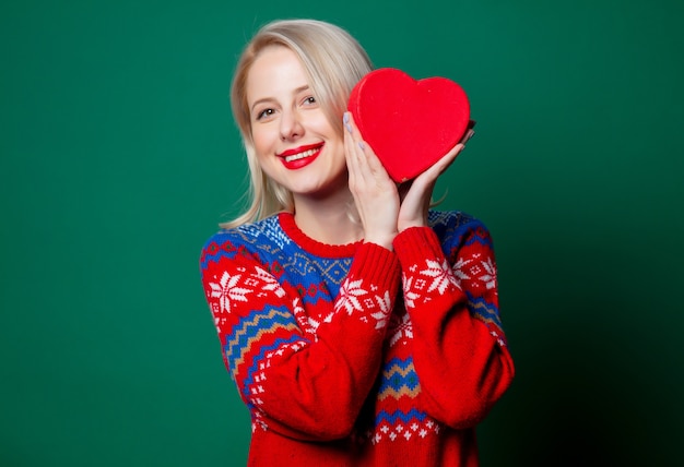 Hermosa mujer en suéter de Navidad con caja de regalo en forma de corazón