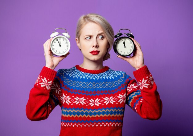 Hermosa mujer en suéter de Navidad con reloj despertador