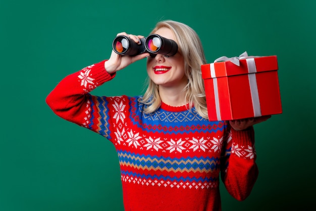 Hermosa mujer en suéter de Navidad tiene caja de regalo y binoculares