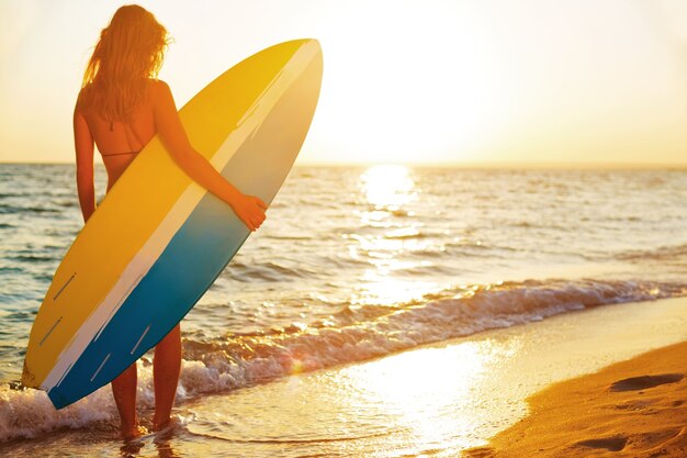 Hermosa mujer surfista en la playa al atardecer