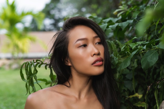 Hermosa mujer tailandesa asiática con piel suave, limpia, bronceada oscura, belleza, retrato, cuidado de la piel, positivo, posando con hojas verdes, labios carnosos, belleza natural al aire libre