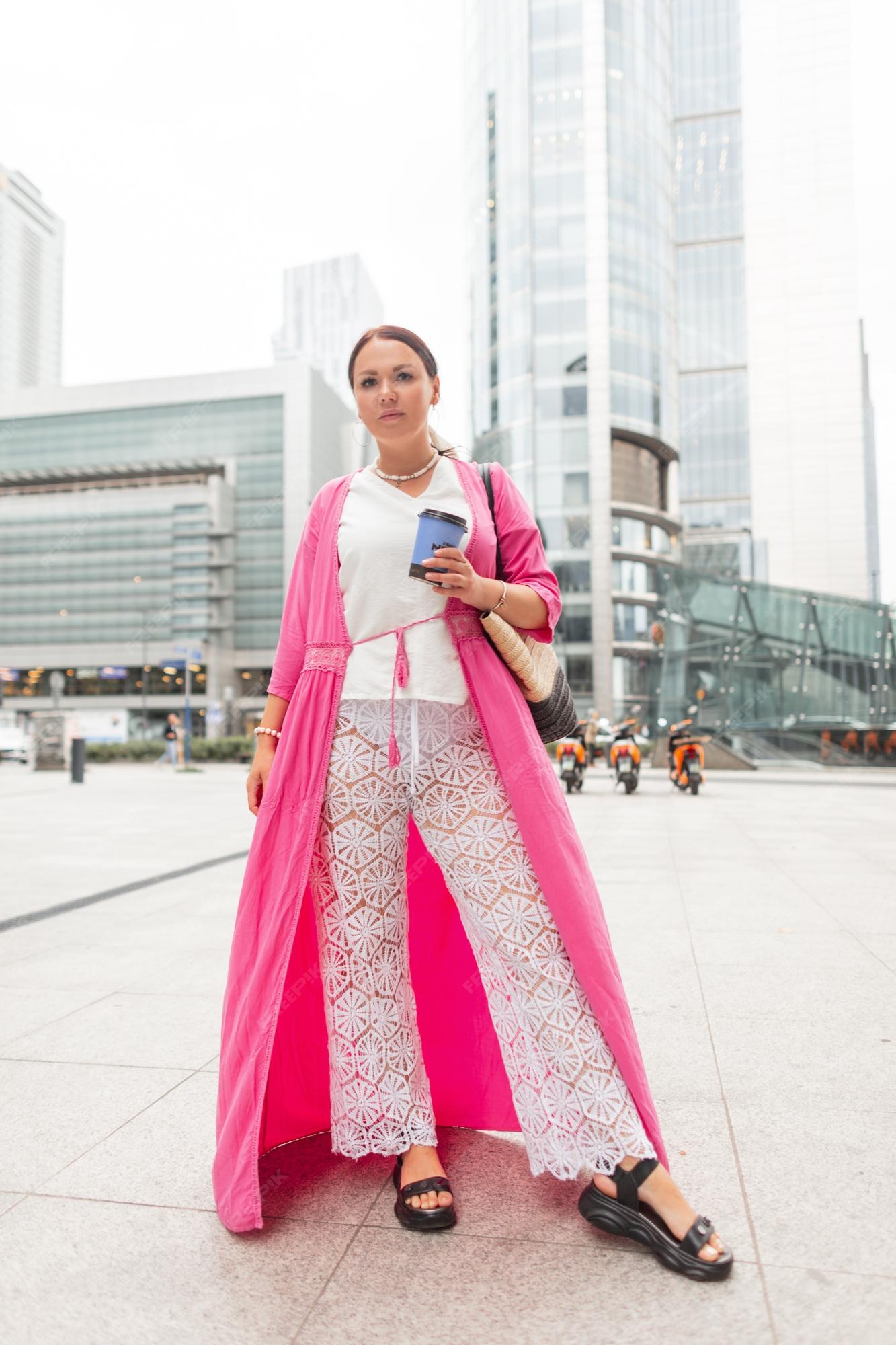 Hermosa mujer de talla grande a moda con elegante ropa de verano con rosa y pantalones de encaje blanco camina por la ciudad y bebe café | Foto Premium