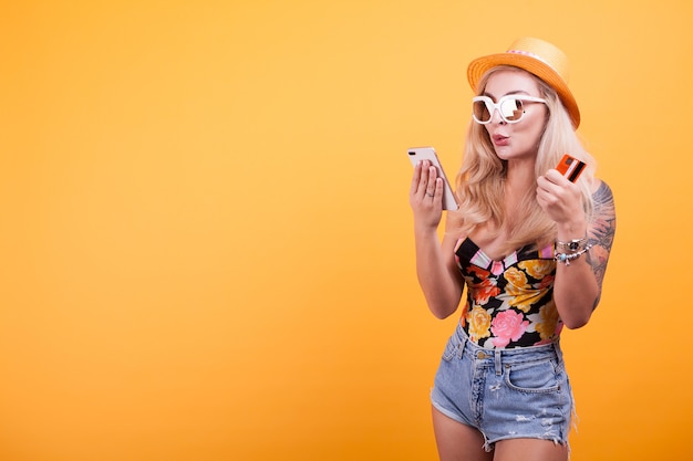 Hermosa mujer tiene teléfono inteligente y tarjeta de crédito en estudio sobre fondo amarillo