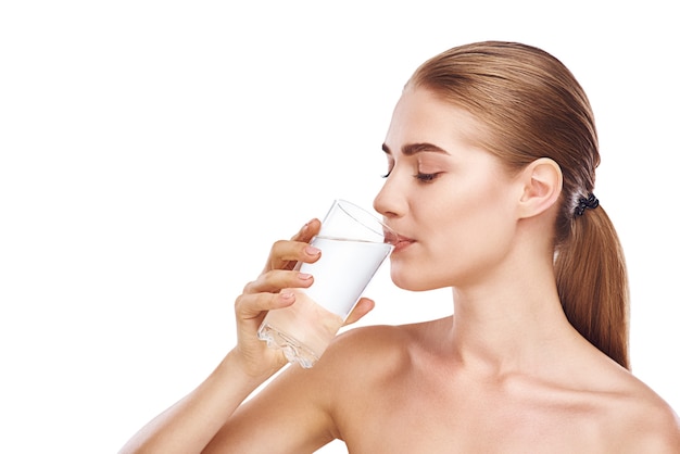 Hermosa mujer en toalla está bebiendo vaso de agua foto de estudio de primer plano sobre fondo blanco. Cabello claro, ojos grises