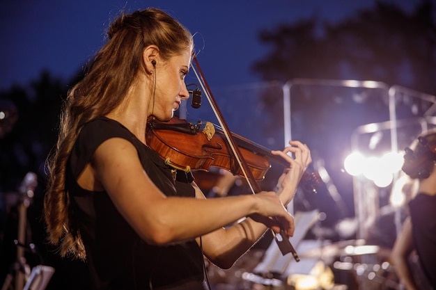 Hermosa mujer tocando el violín en el concierto al aire libre de noche