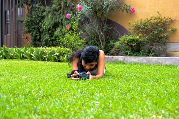 Hermosa mujer tomando fotos con una cámara digital, tumbada en la vegetación.