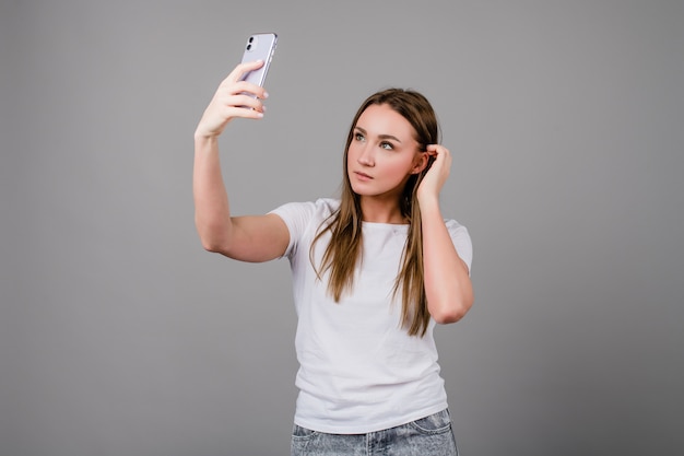 Hermosa mujer tomando selfie en un teléfono sobre fondo gris