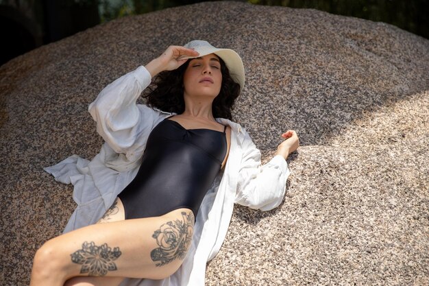 Foto hermosa mujer tomando el sol, mujer con sombrero apoyado en una roca al aire libre, vacaciones de verano