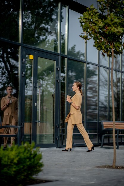 Hermosa mujer va a trabajar con café caminando cerca del edificio de oficinas