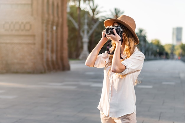 Hermosa mujer en traje de explorador viajando y tomando fotografías con cámara vintage.