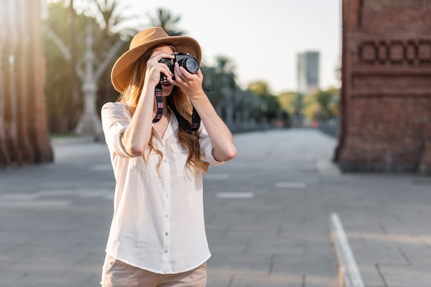 Hermosa mujer en traje de explorador viajando y tomando fotografías con cámara vintage.