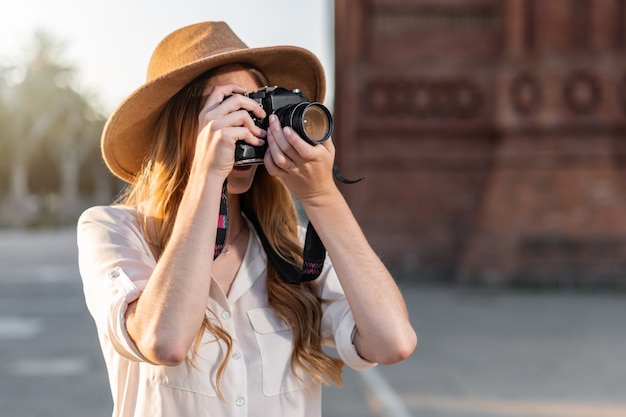 Hermosa mujer en traje de explorador viajando y tomando fotografías con cámara vintage.