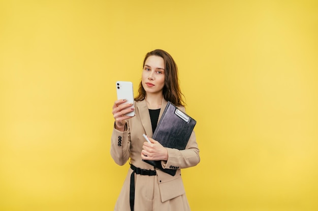 Hermosa mujer en un traje con una tableta y un teléfono inteligente en sus manos se encuentra sobre un fondo amarillo