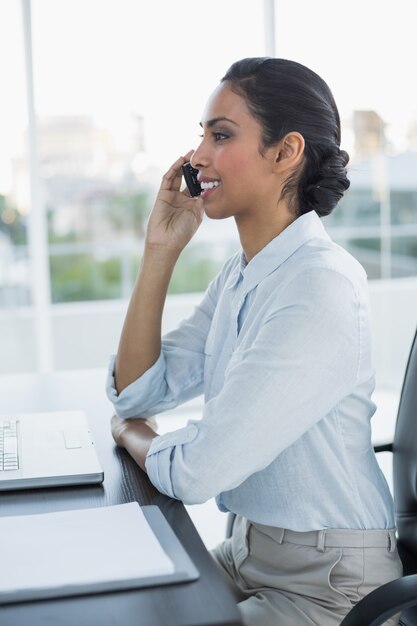 Hermosa mujer tranquila llamando con su teléfono inteligente sentado en su escritorio