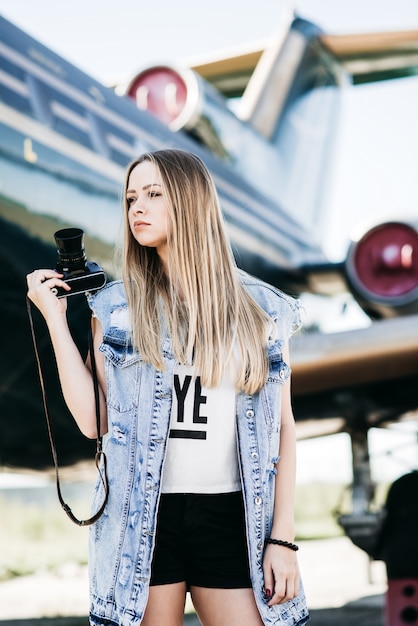 Hermosa mujer turística con cámara vieja película vintage posando cerca del avión