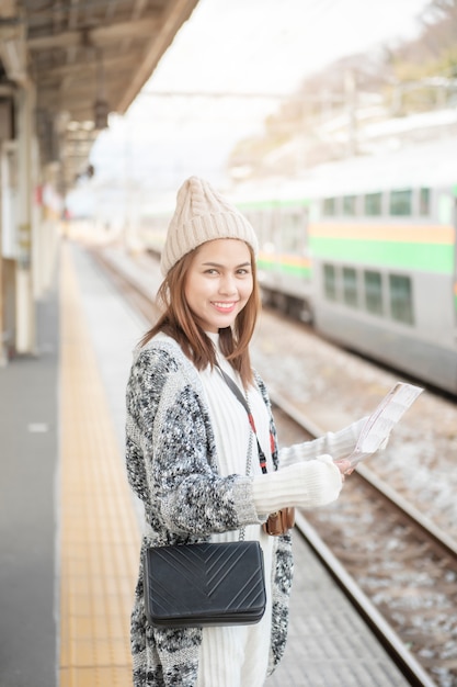 Hermosa mujer turística está de pie en la plataforma del ferrocarril con su mapa