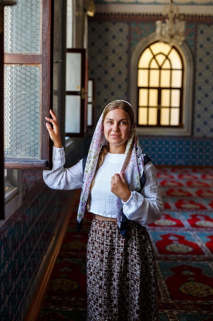 Una hermosa mujer ucraniana con un pañuelo en la cabeza se para en la mezquita junto a la ventana y reza por la paz