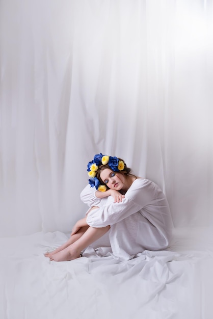 Hermosa mujer ucraniana con un vestido blanco y una corona floral sobre fondo blanco Símbolo de la bandera azul amarilla ucraniana La dama tranquila está dormida Paz en Ucrania