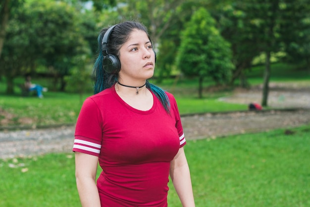 Hermosa mujer universitaria con cabello azul y vestido rojo escuchando música con sus auriculares inalámbricos