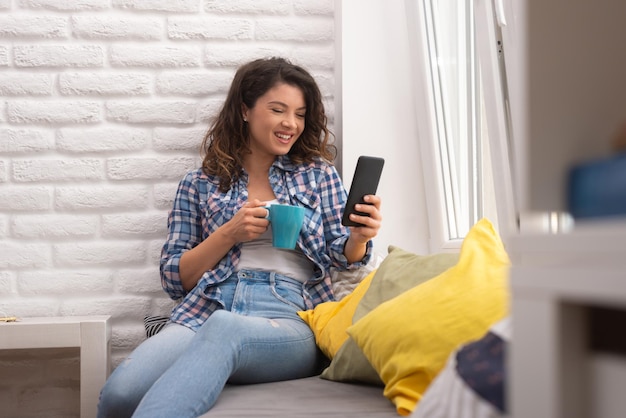 Hermosa mujer usando el teléfono para revisar sus mensajes Bebiendo café y usando el teléfono