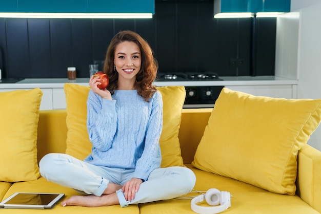 Hermosa mujer vegetariana en ropa casual sostiene una manzana roja fresca mientras está sentada en cómodo