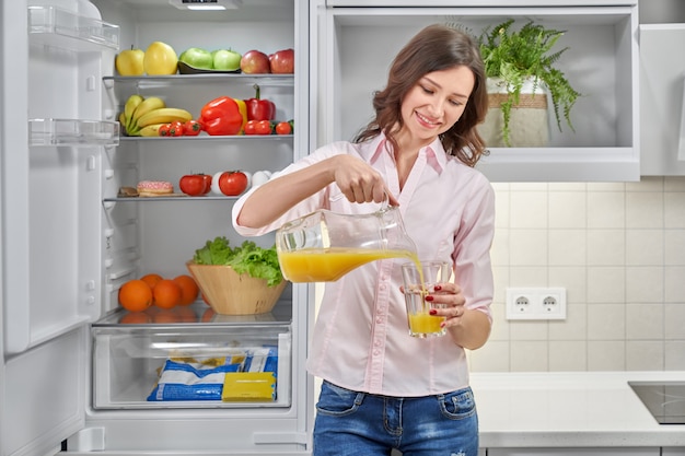 Hermosa mujer vertiendo jugo de naranja fresco en vidrio