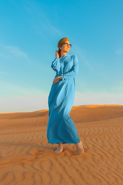 Hermosa mujer vestida de azul entre el desierto de Dubái al atardecer