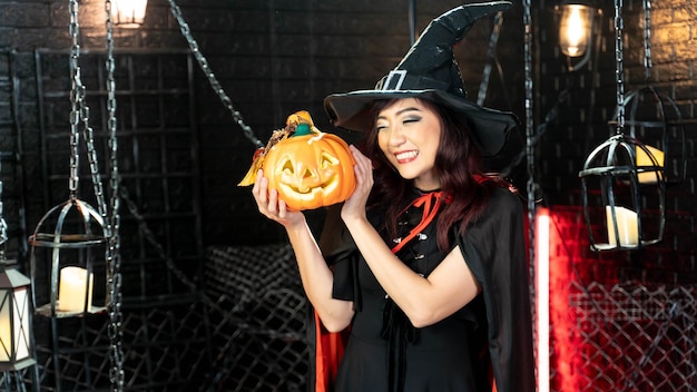 Hermosa mujer vestida de bruja para Halloween con linterna de calabaza en el tema de Halloween